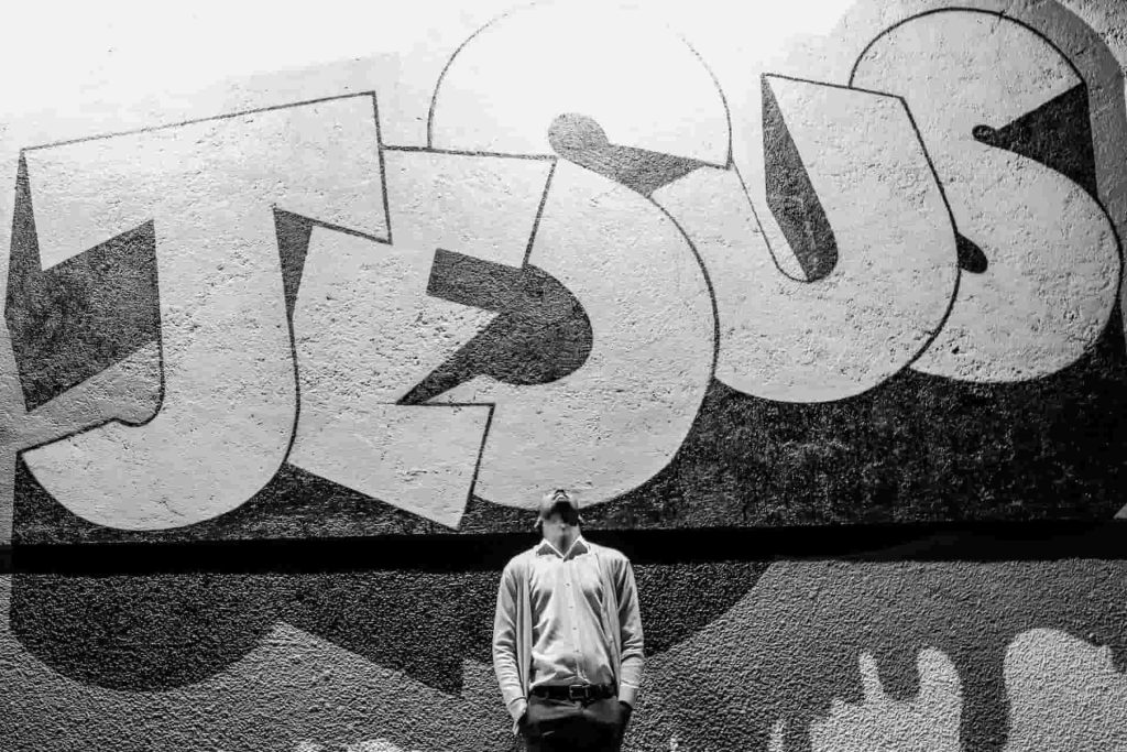 A man standing under a Jesus Street Art, and looking up