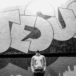 A man standing under a Jesus Street Art, and looking up